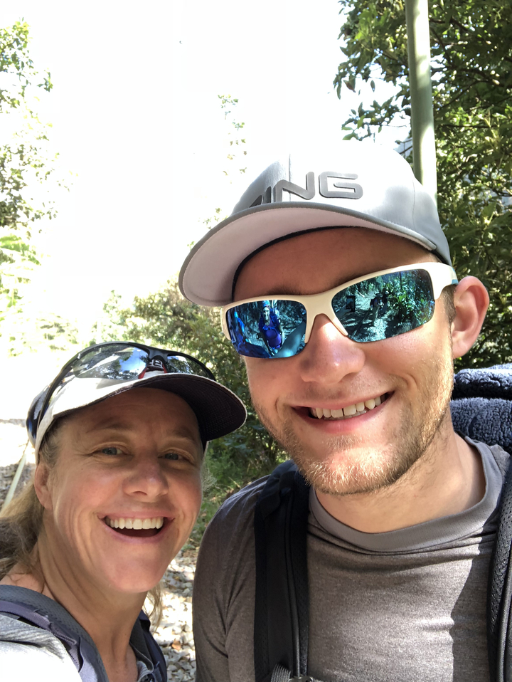 Gros plan souriant d'une personne portant des lunettes de soleil reflétant la nature.