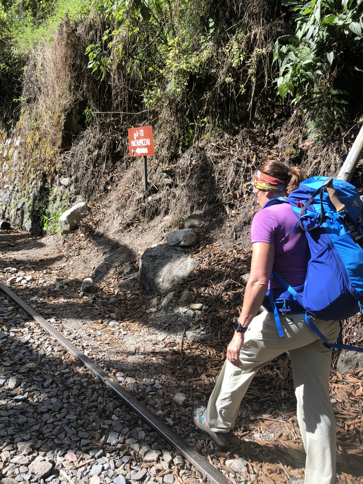 Randonneur marchant le long d'une voie ferrée avec un panneau indiquant la gauche.