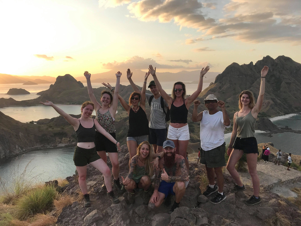 Group of people celebrating on a hill with a scenic sunset.