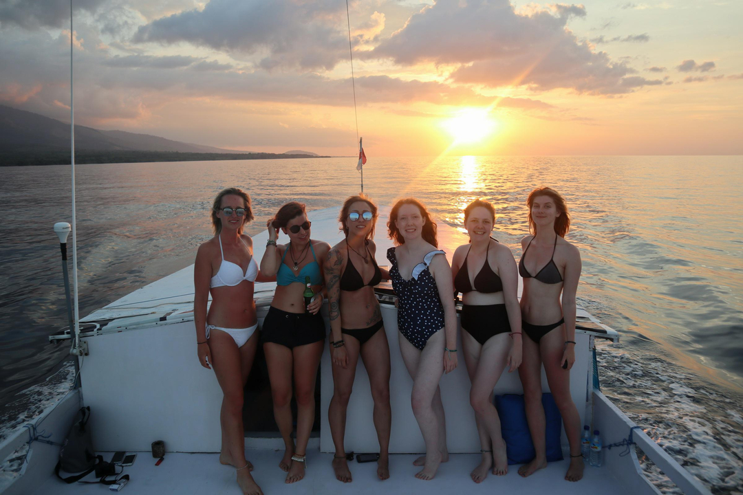 Six women posing on a boat during sunset.