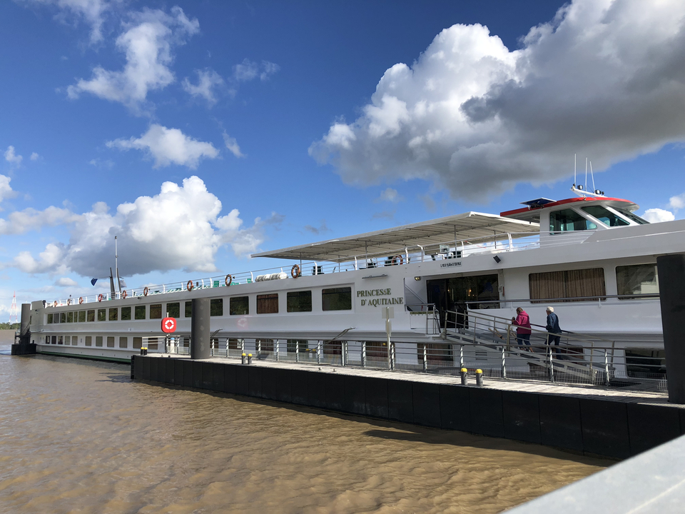Un grand bateau de croisière fluviale accoste dans un ciel bleu et des nuages.