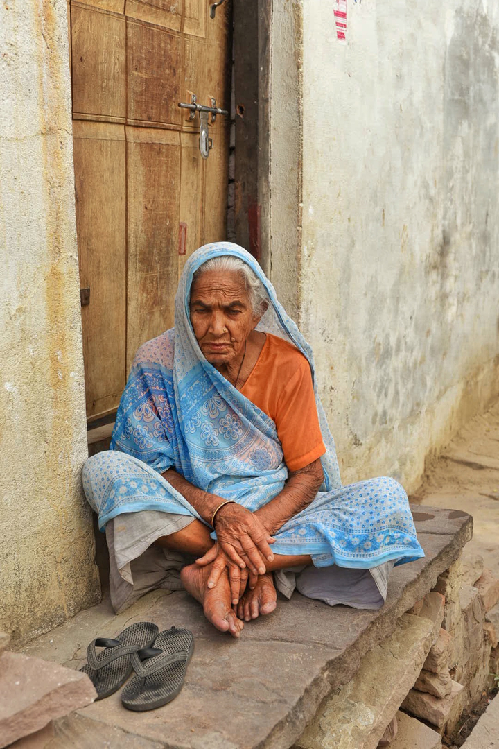 Femme âgée assise sur le seuil d'une porte, vêtue d'un sari traditionnel.