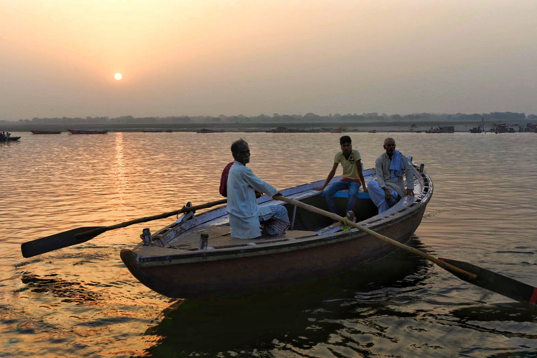 Trois hommes ramant sur un bateau lors d'un coucher de soleil sur une rivière.