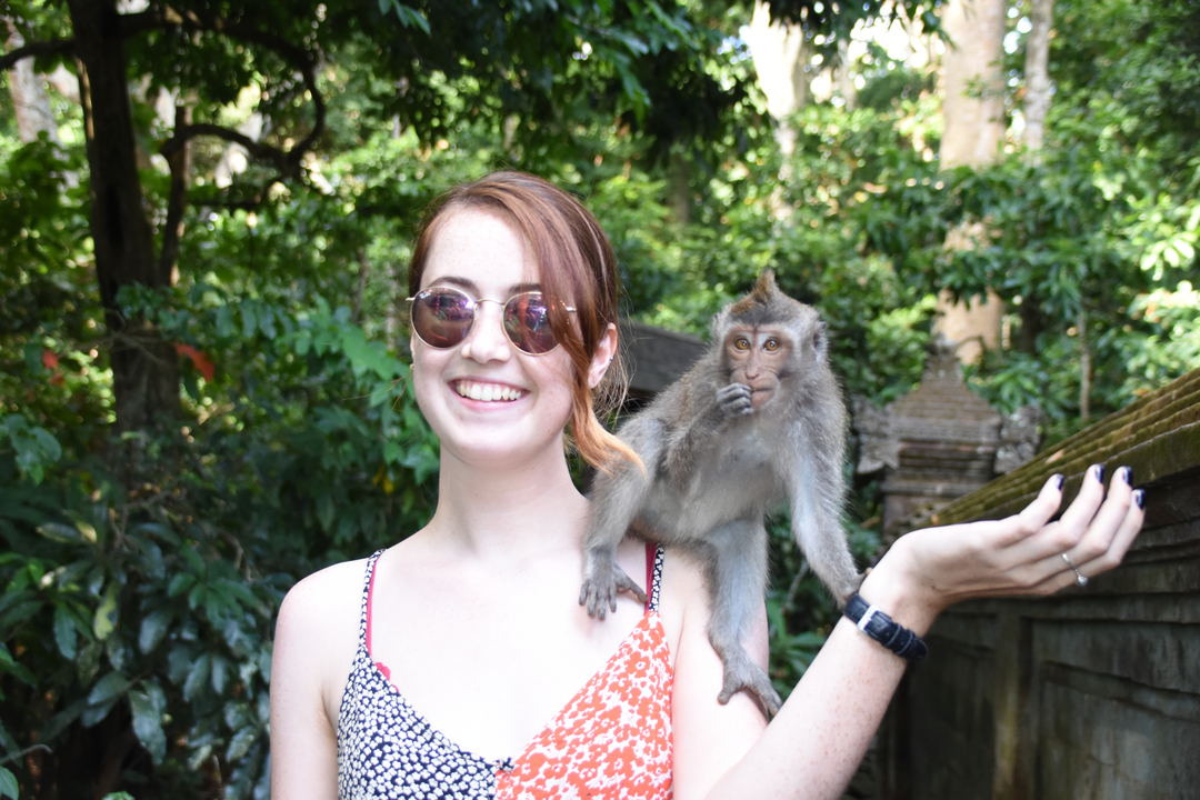 Woman posing with a monkey on her shoulder in a forest.