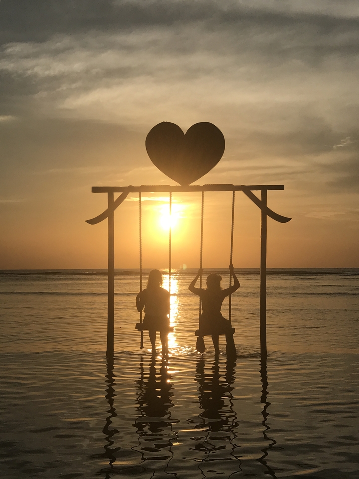 Silhouette of two people on a swing set against a sunset backdrop on the beach.