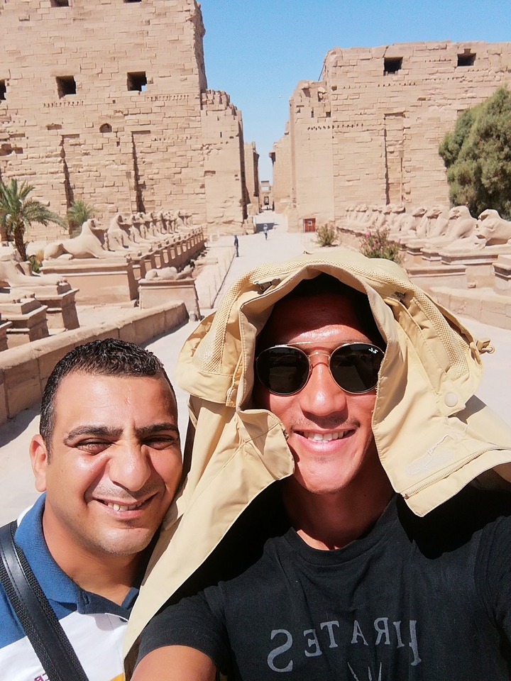 Des hommes souriants posent devant une ancienne avenue égyptienne.