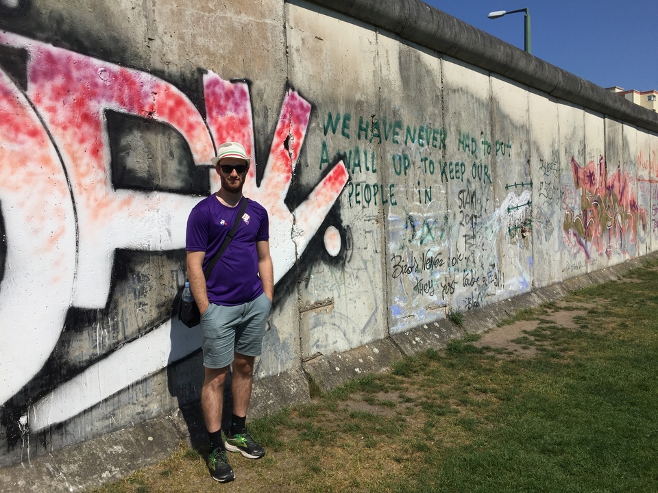 Homme debout devant une partie du mur de Berlin recouverte de graffitis.