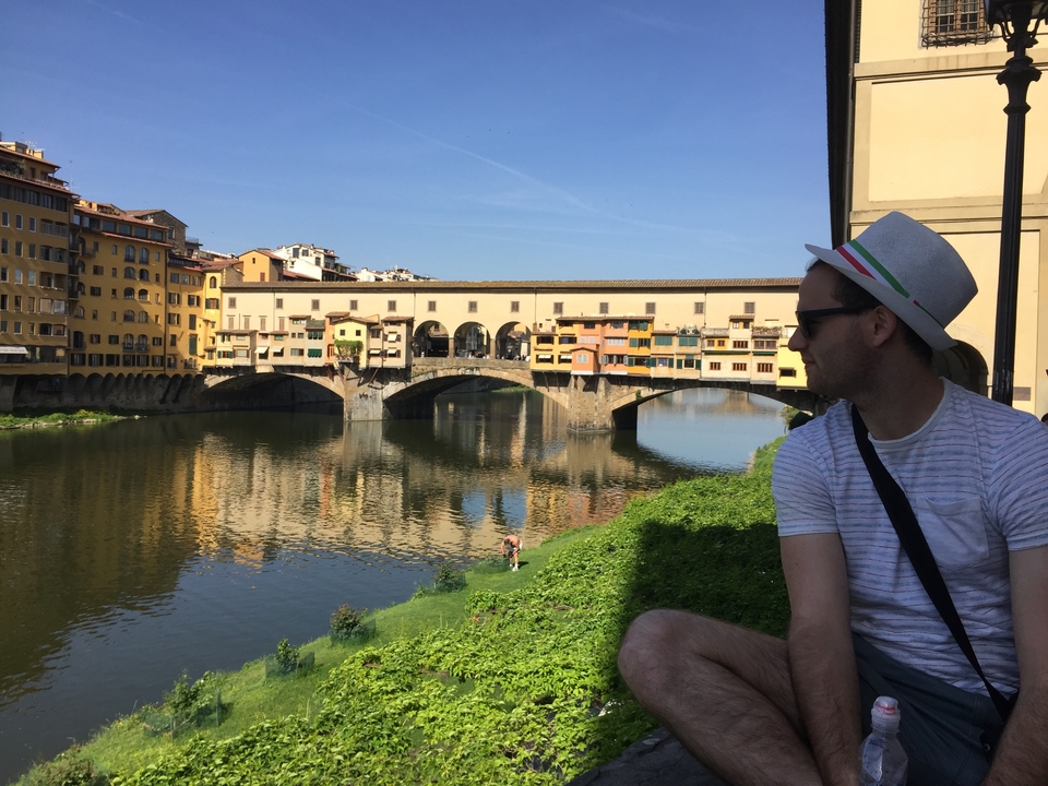 Homme assis au bord de la rivière avec le Ponte Vecchio en arrière-plan.