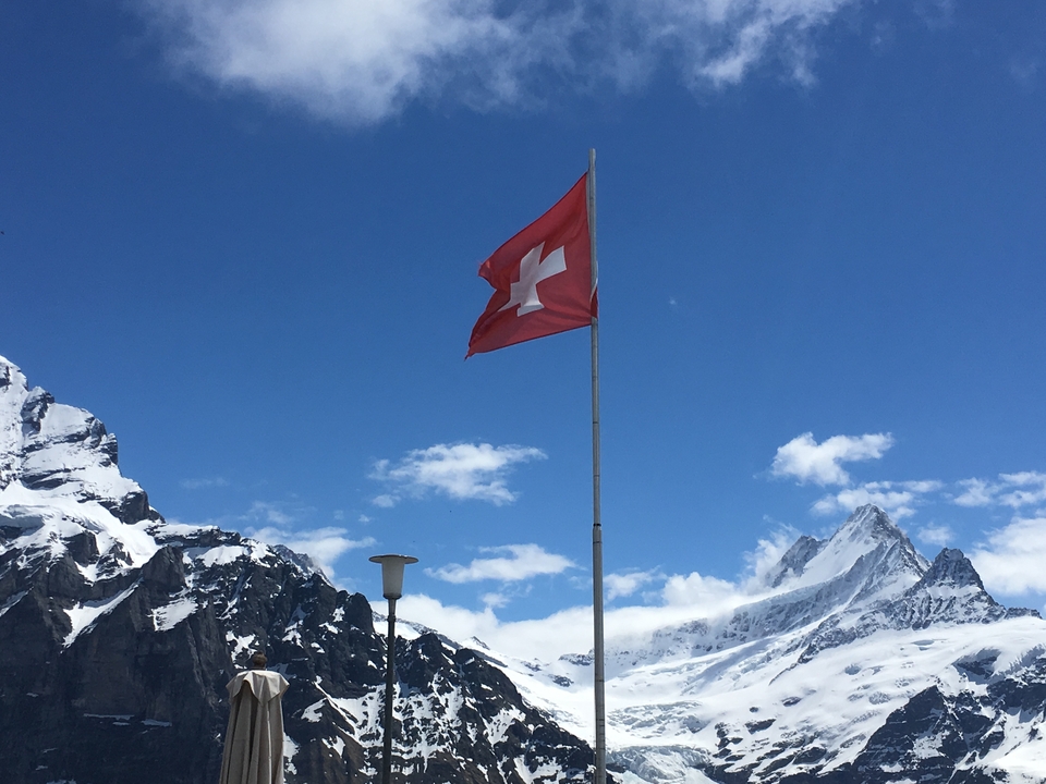 Die Schweizer Flagge weht über schneebedeckten Bergen.