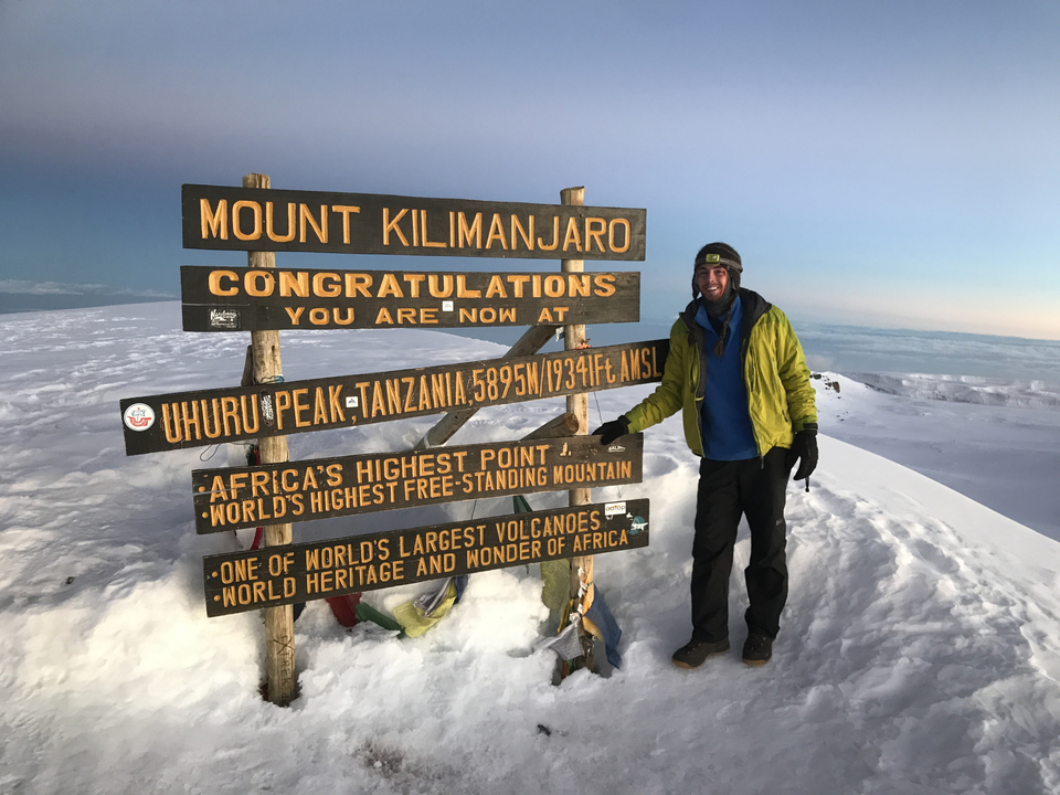 Une personne se tenant près du panneau indiquant le sommet du mont Kilimandjaro.