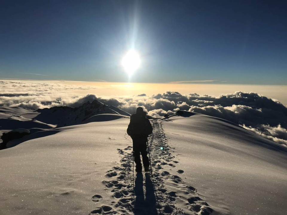 Une personne faisant du trekking sur une montagne enneigée avec un lever de soleil époustouflant.