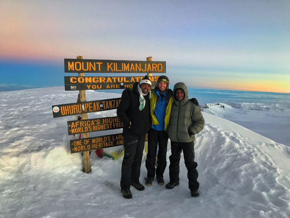 Trois personnes posant devant le panneau indiquant le sommet du pic Uhuru sur le mont Kilimandjaro.