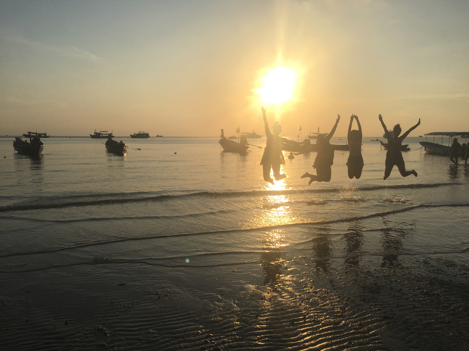 Silhouetted group jumping on a beach at sunset.