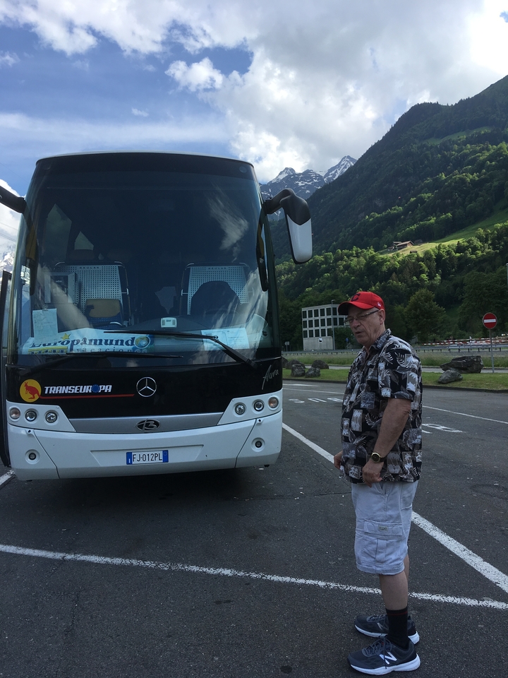 Homme debout à côté d'un bus de tourisme dans un parking.
