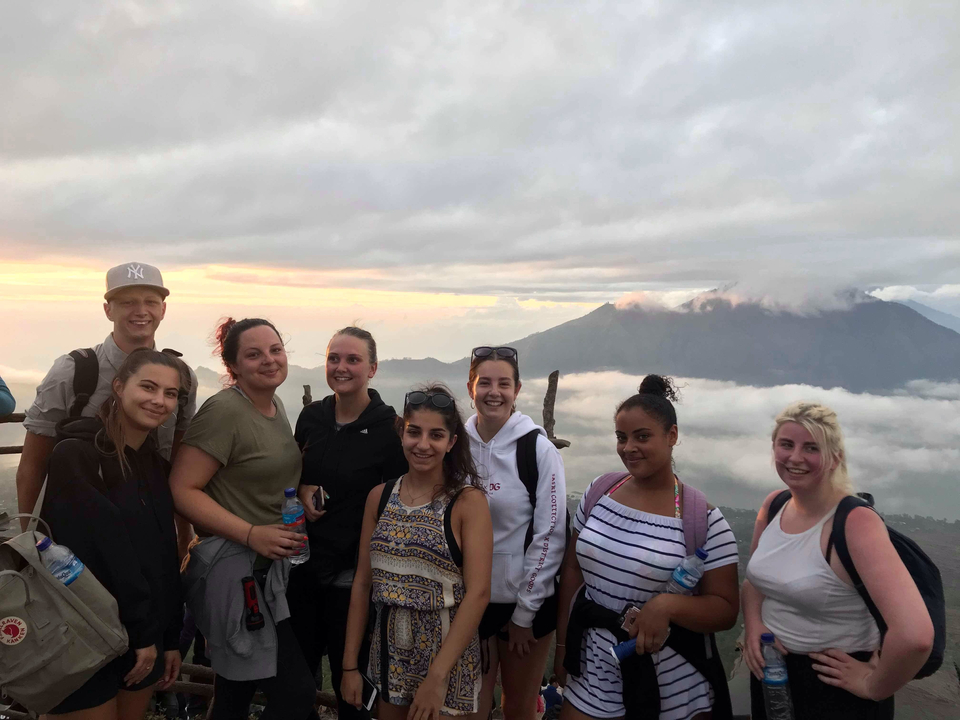 Group of people smiling with a mountain view and clouds in the background.