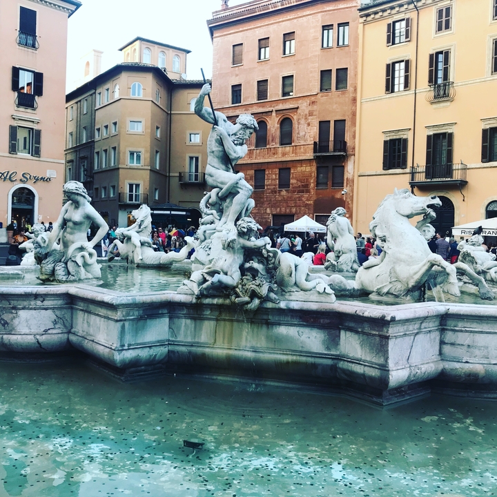 Fontaine sculpturale avec des sculptures complexes représentant des figures mythiques sur une place animée.