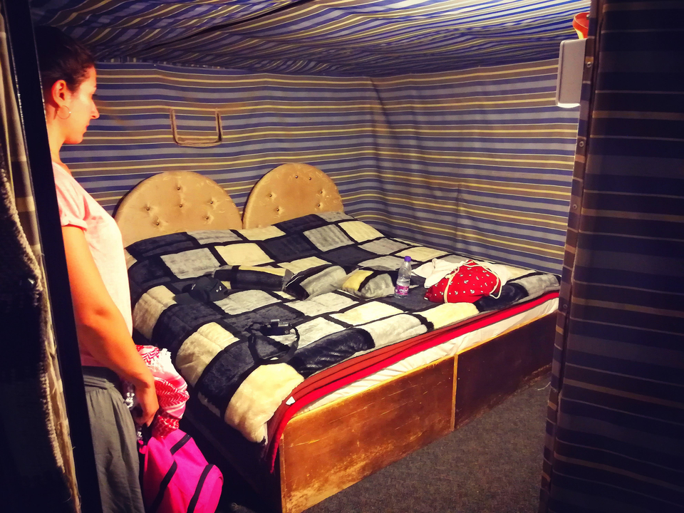 Femme debout dans une tente avec un lit bien fait et un décor orné.