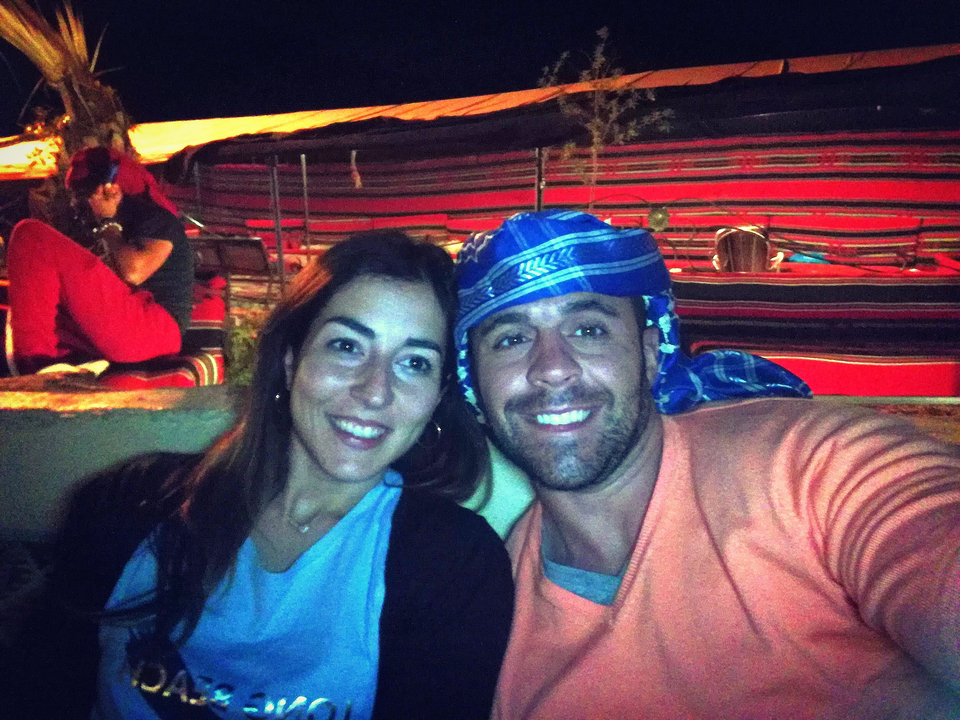 Deux personnes posant avec des couvre-chefs en tissu coloré dans une tente.