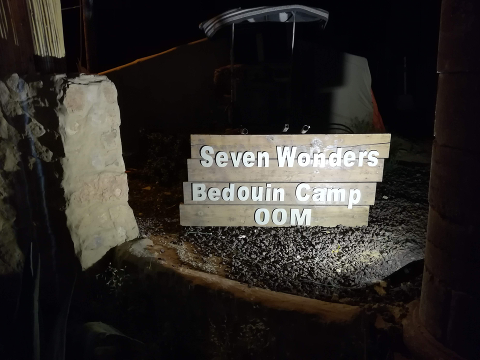 Panneau indiquant "Seven Wonders Bedouin Camp" à côté d'un chemin rocailleux.