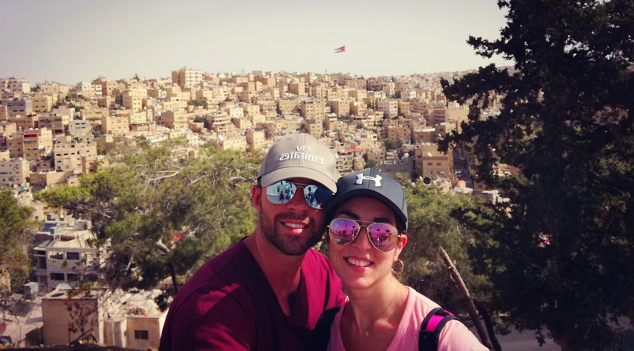 Couple posant devant un paysage urbain composé de nombreux bâtiments beiges.