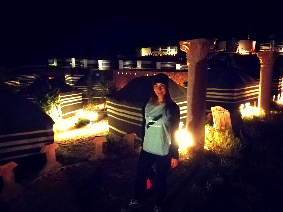 Femme parmi les tentes illuminées du désert avec des colonnes la nuit.