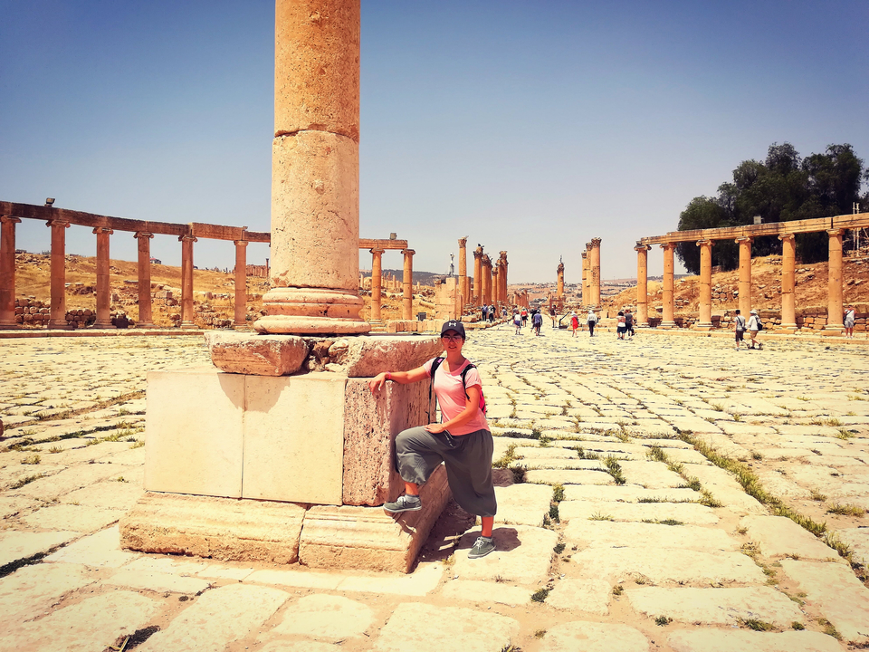 Personne posant avec une colonne ancienne dans une grande zone de ruines ouverte.