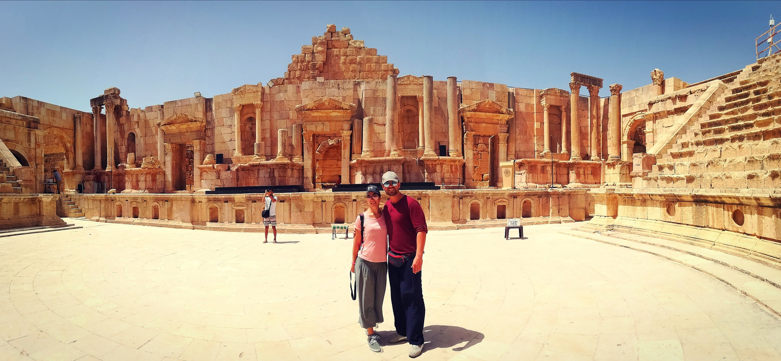 Couple debout devant un théâtre antique en pierre.