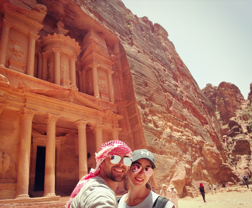Couple devant une architecture ancienne sculptée dans la roche sous un ciel ensoleillé.