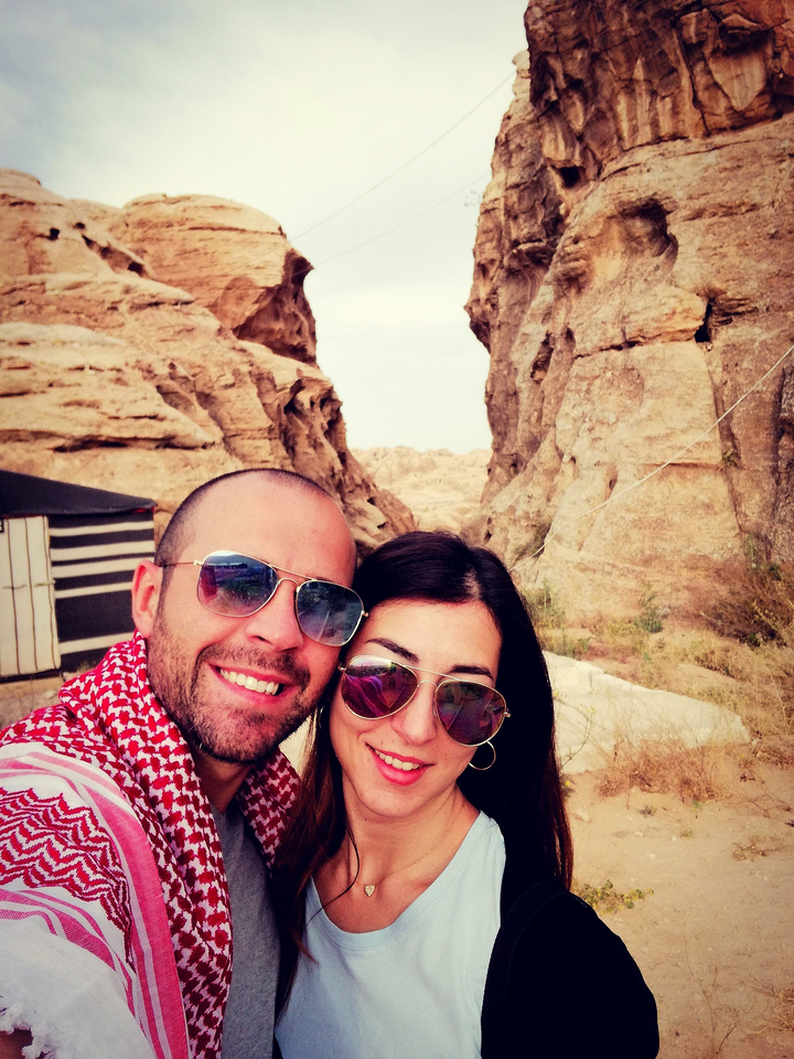 Couple taking a selfie with desert landscape and traditional tent in the background.