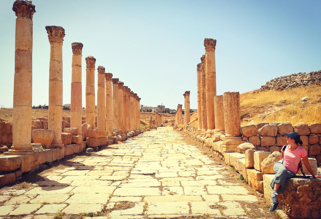 Personne marchant le long d'une ancienne allée bordée de colonnes romaines.