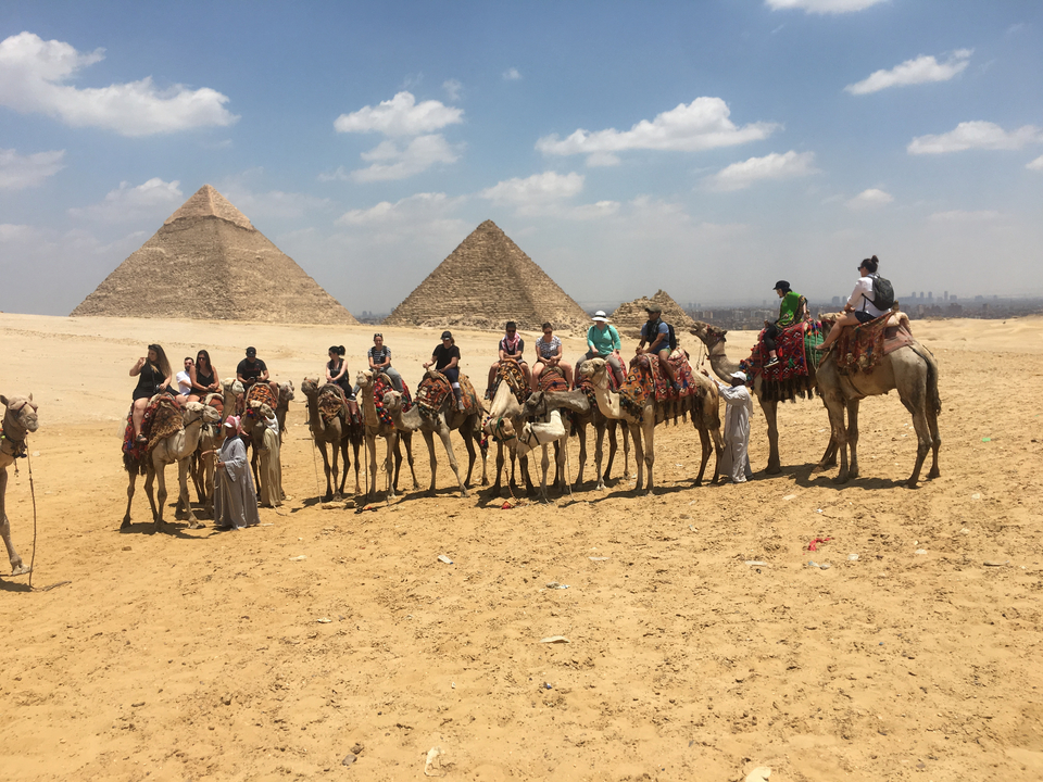 Groupe de personnes à dos de chameau devant des pyramides dans le désert.