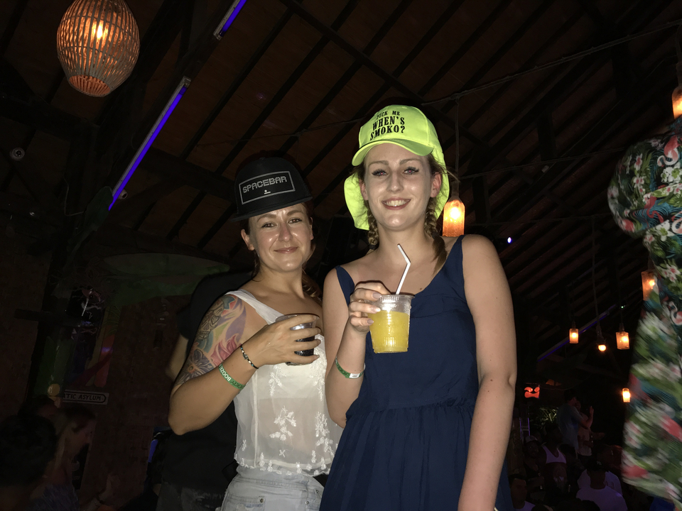 Two people posing indoors with drinks, wearing hats.