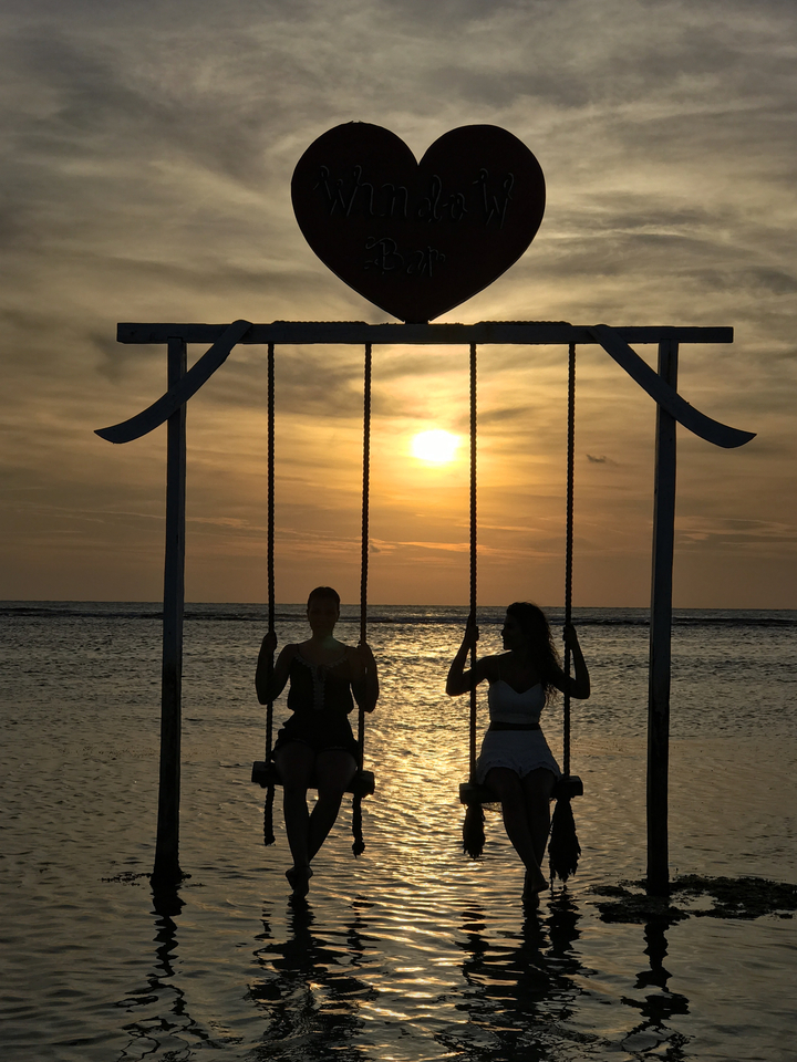 Two people on a beach swing at sunset.