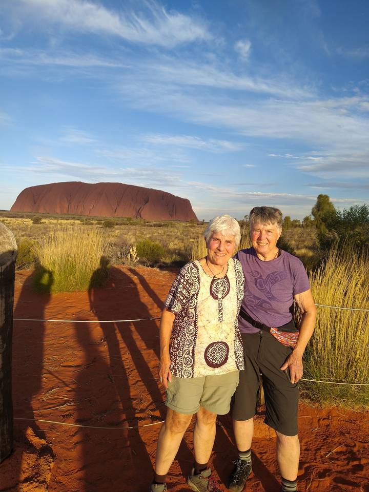 Deux personnes assises devant un monolithe de roche rouge.