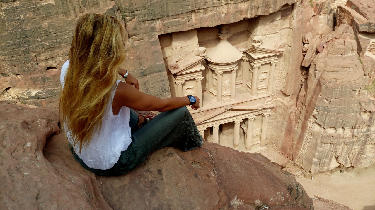 Une personne assise sur une falaise surplombant le Trésor de Petra.
