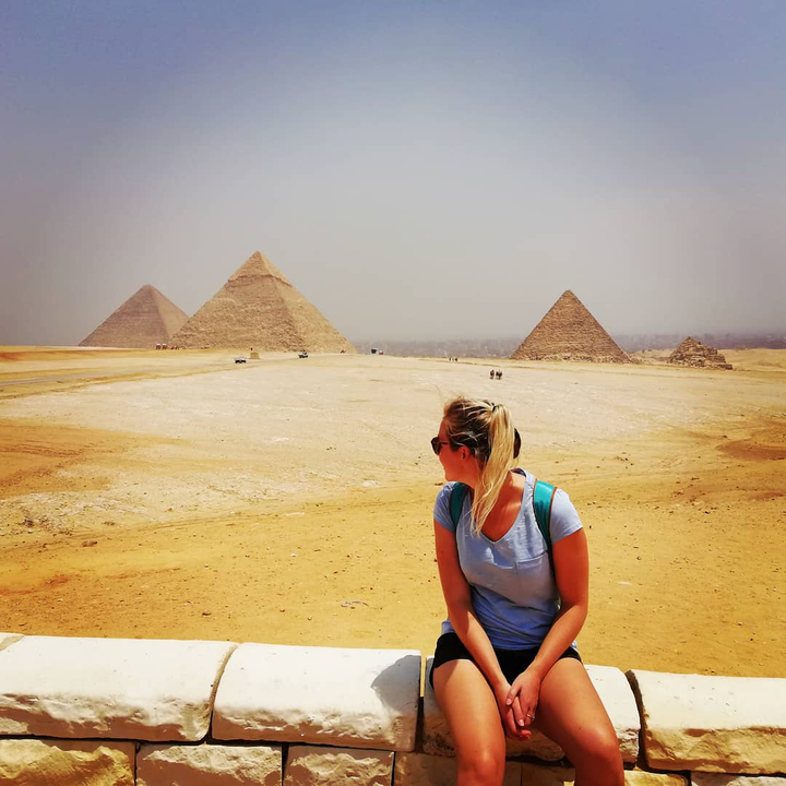 A woman overlooking the pyramids of Giza under a hazy sky.