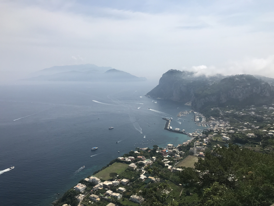 Vue aérienne d'une zone côtière avec des bateaux et des îles lointaines dans un ciel brumeux.