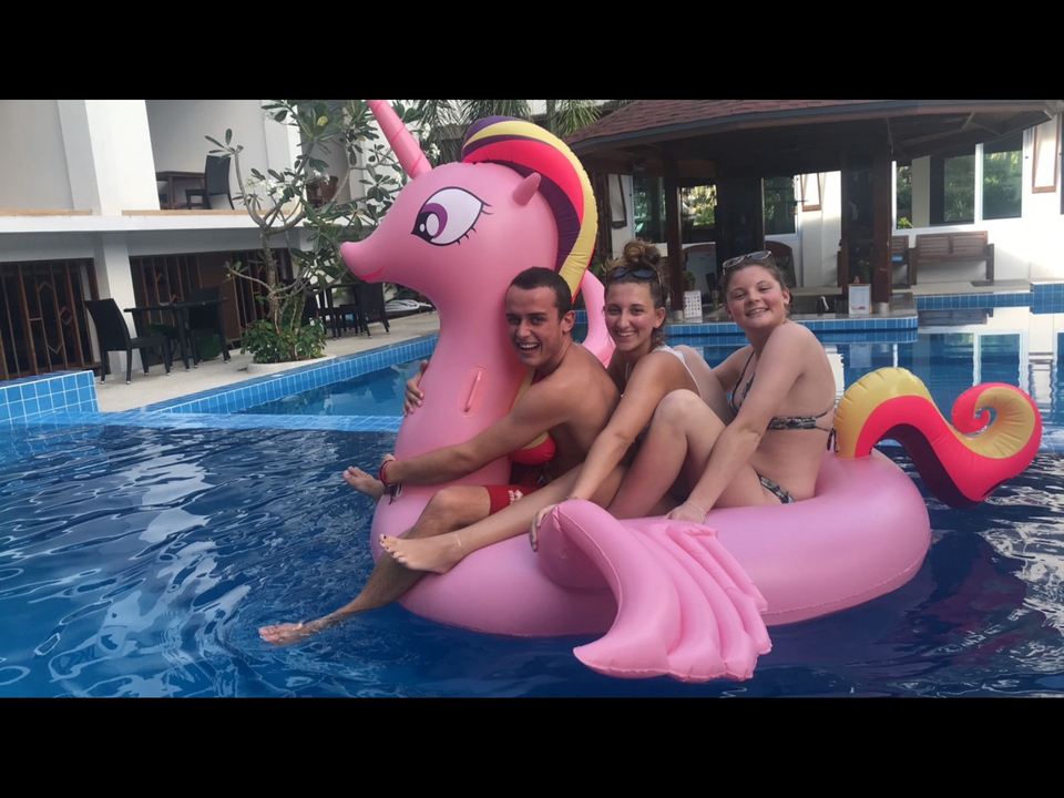 Three people on a pink inflatable in a pool.