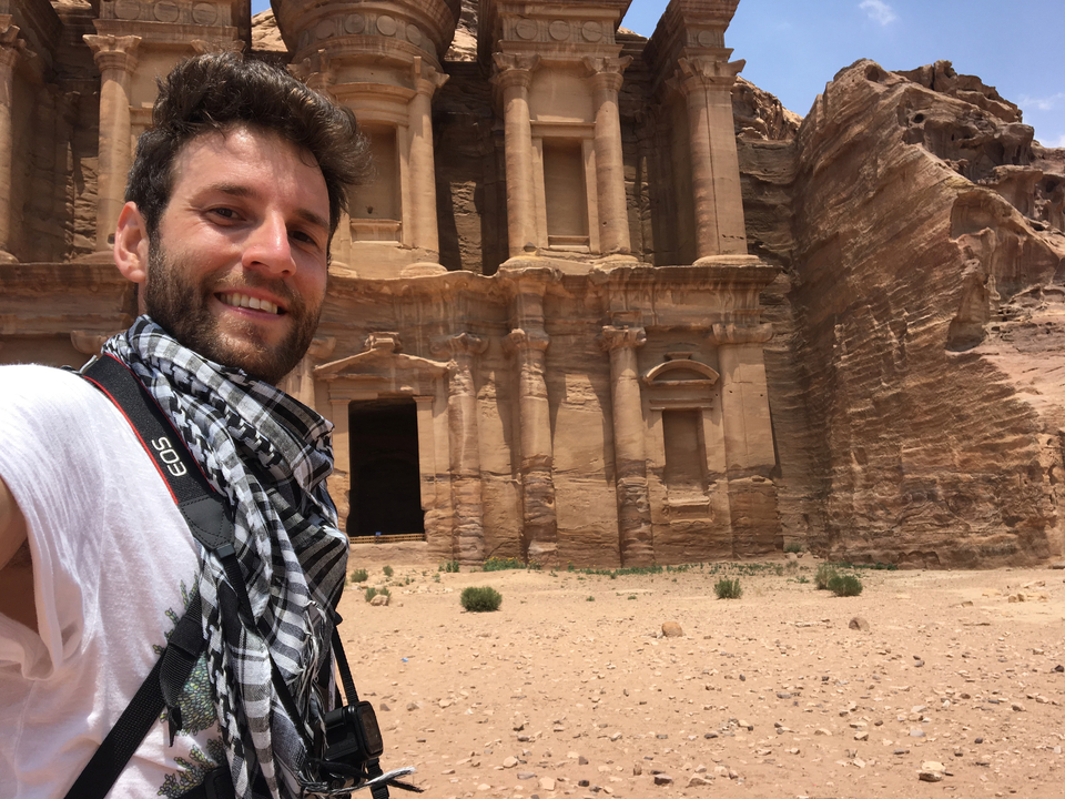 Homme prenant un selfie avec l'ancienne Petra sculptée dans la roche en arrière-plan.