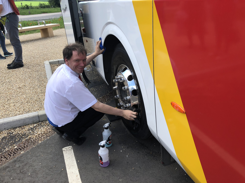 Personne nettoyant la roue d'un grand bus sur un parking.