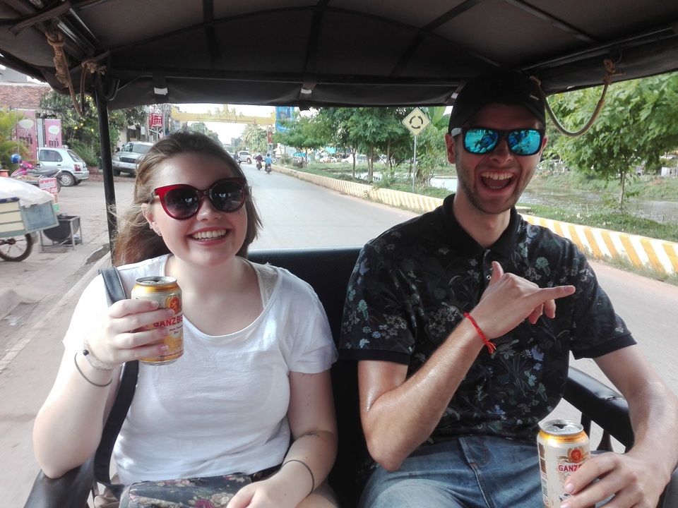 Deux personnes souriant et tenant des boissons à bord d'un tuk-tuk.