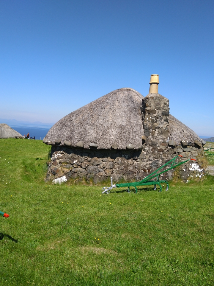 Maison ronde en pierre à toit en chaume sur une colline herbeuse.