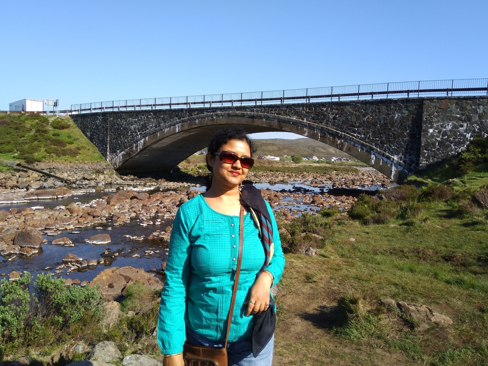 Femme posant près d'un pont de pierre avec la rivière en contrebas.