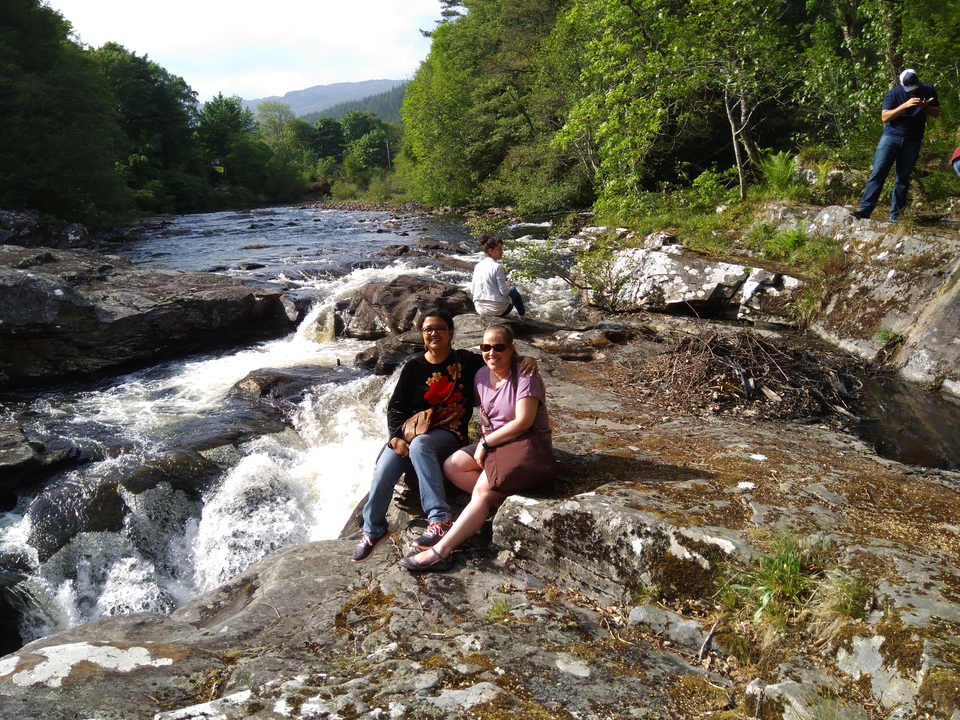 Deux femmes assises au bord d'une rivière aux rives rocheuses.
