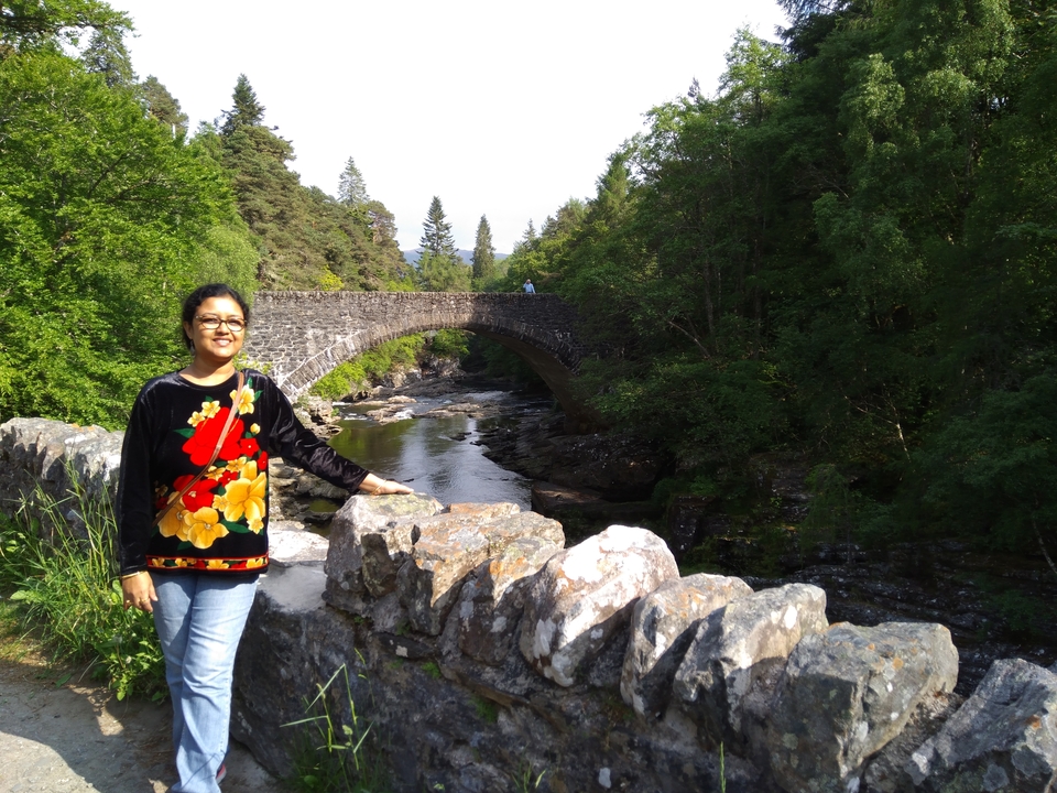 Personne debout près d'un pont de pierre enjambant un ruisseau.