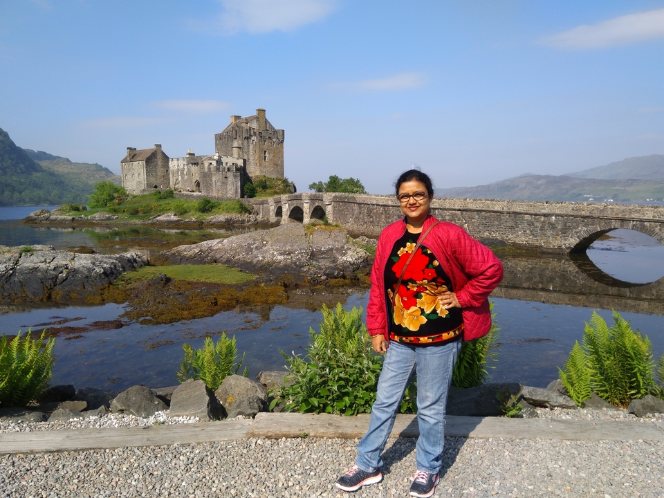 Femme debout près du château d'Eilean Donan et d'un pont de pierre.