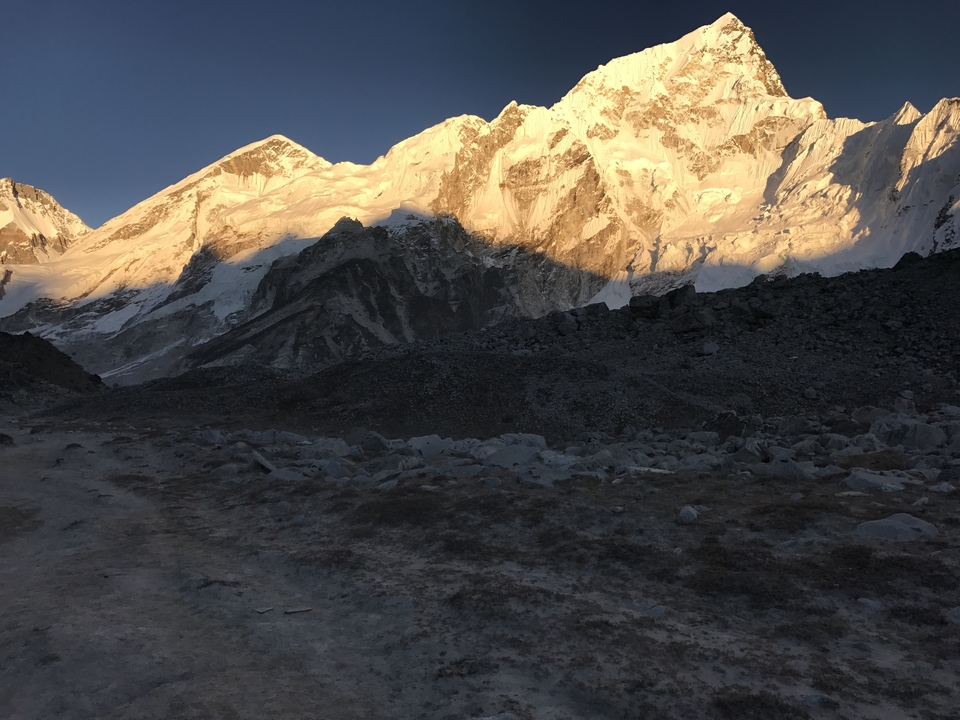 Golden light strikes the upper flanks of towering Himalayan summits while the foreground remains in deep shadow.