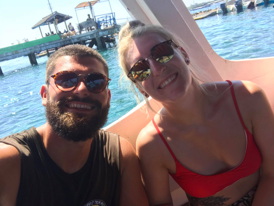 Two people smiling on a boat with blue water in the background.