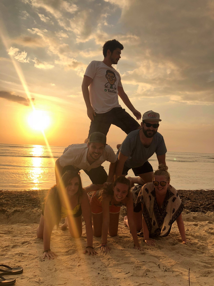 People forming a human pyramid on the beach during sunset.