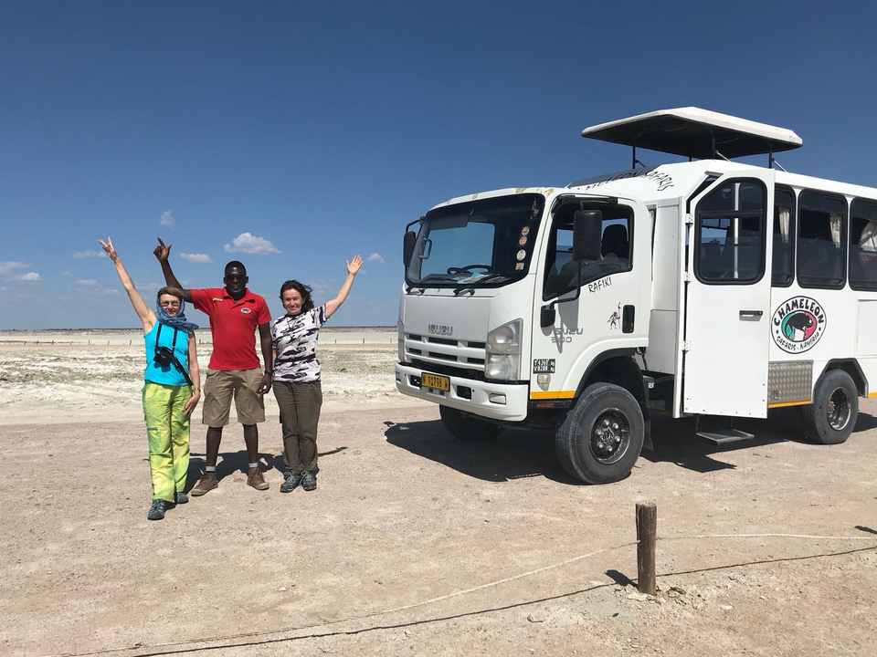 Trois personnes posant à côté d'un véhicule de safari sur fond de savane.